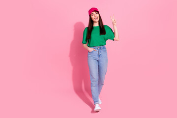 Full length photo of cheerful pretty lady dressed green t-shirt pink headwear showing v-sign empty space isolated pink color background