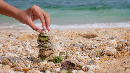 human hands putting the last coral stone on the pyramid, white sand beach with summer atmosphere, activities every on the beach