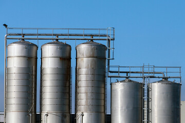 Shiny metal tanks placed in a row under clear blue sky