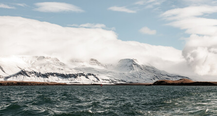 Coastal Icelandic landscape with snowy mountains under cloudy sky
