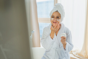 Mature adult old woman applying nourishing anti age face cream doing daily beauty routine. Senior woman with white mask or creme on skin gets facial treatment Skin care aging beauty skincare cosmetics