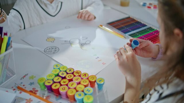 Small child examining stamp creating art in school closeup. Schoolgirl drawing