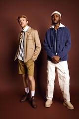 Two handsome multicultural men with stylish clothing standing together against a brown background.