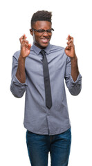 Fototapeta premium Young african american business man over isolated background smiling crossing fingers with hope and eyes closed. Luck and superstitious concept.