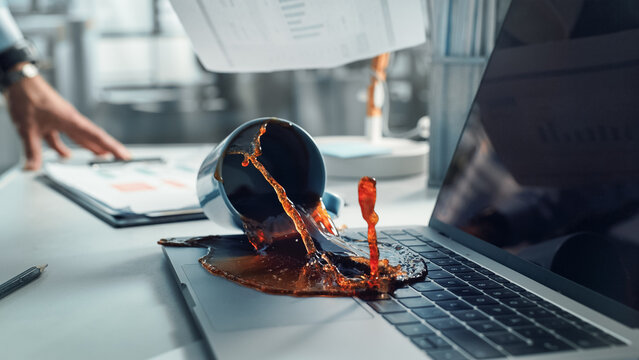 Office Manager Accidentally Spilling Hot Coffee on Working Laptop Computer with Business Presentation Or Financial Reports For Large Company. Concept of Failing or Screwing Up In A Workplace