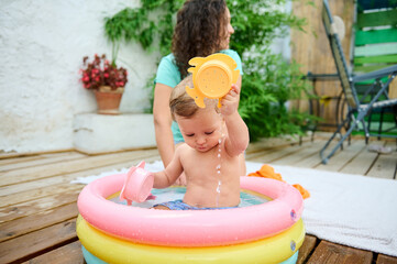Adorable baby playing with water in a backyard inflatable pool on a sunny day