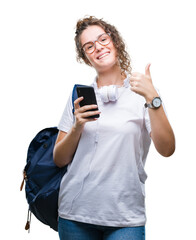 Young brunette student girl wearing backpack, headphones and smartphone over isolated background happy with big smile doing ok sign, thumb up with fingers, excellent sign