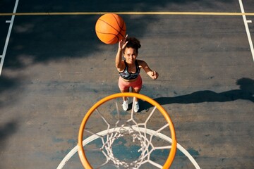 Practice like youve never won, play like youre never lost. High angle shot of a sporty young woman throwing a basketball into a net on a sports court.