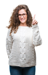 Beautiful brunette curly hair young girl wearing winter sweater over isolated background showing and pointing up with finger number one while smiling confident and happy.