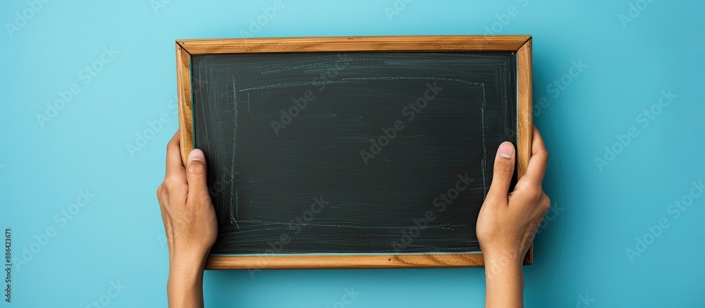 Poster Hand holding a blank chalkboard against a blue backdrop with space for text or images. with copy space image. Place for adding text or design
