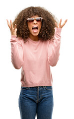 African american woman wearing pink sunglasses celebrating mad and crazy for success with arms raised and closed eyes screaming excited. Winner concept