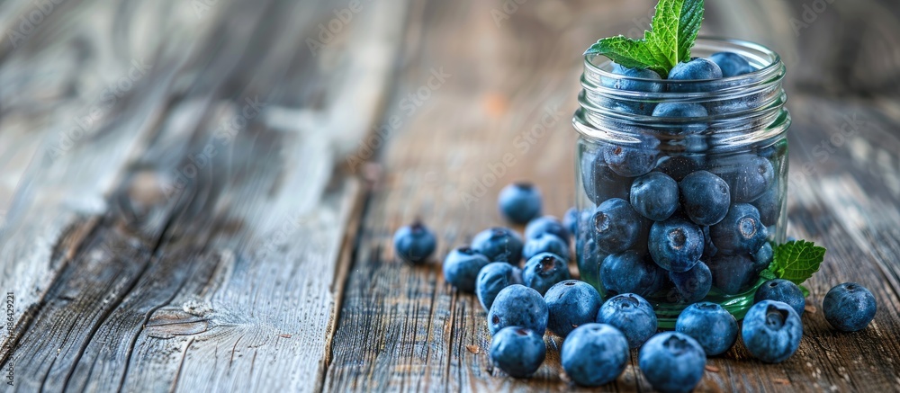 Poster A jar filled with blueberries topped with a mint leaf placed on an aged wooden table with ample copy space image