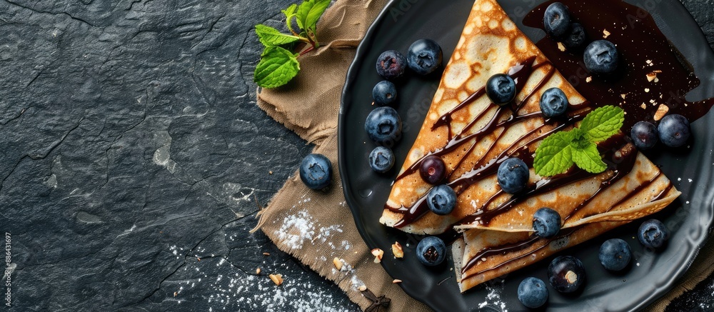 Poster Chocolate crepes with blueberries sauce and mint leaves on a slate plate in a top view shot with a focused area left for text or design known as copy space image