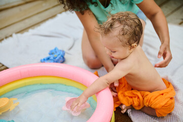 Parent supervising baby playing in inflatable pool outdoors on a sunny day