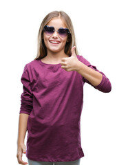 Young beautiful girl wearing sunglasses over isolated background doing happy thumbs up gesture with hand. Approving expression looking at the camera with showing success.