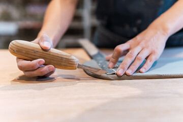 Hands of a precise ceramist is cutting wet clay and modeling it at pottery studio