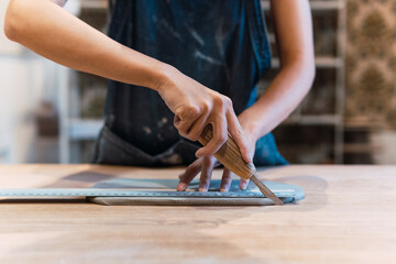 A precise ceramist is cutting wet clay and modeling it at pottery studio