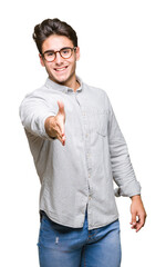 Young handsome man wearing glasses over isolated background smiling friendly offering handshake as greeting and welcoming. Successful business.