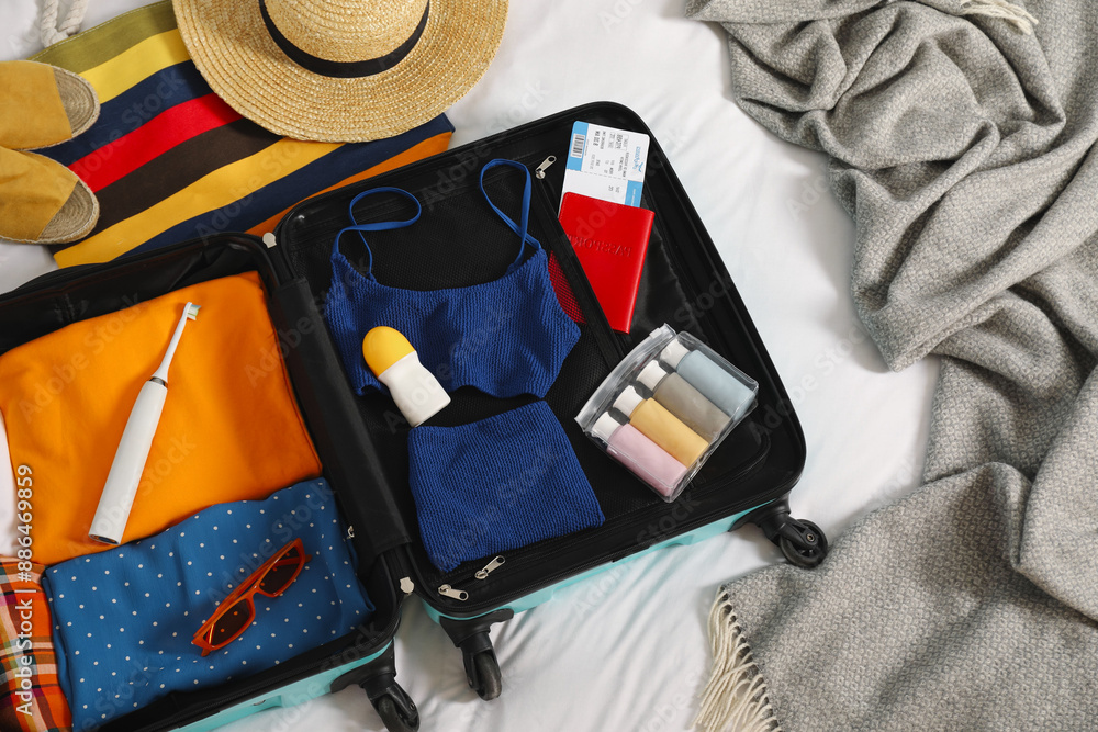 Sticker Open suitcase with traveler's belongings on bed, flat lay