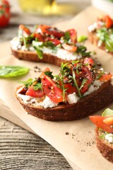 Delicious ricotta bruschettas with tomatoes, arugula and basil on wooden table, closeup