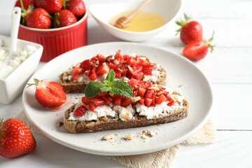 Bruschettas with ricotta cheese, chopped strawberries and mint on white wooden table, closeup