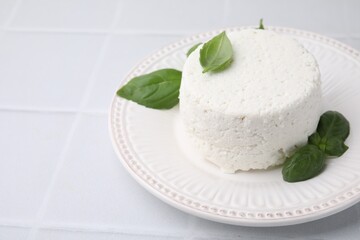 Fresh ricotta (cream cheese) and basil on light tiled table, closeup. Space for text