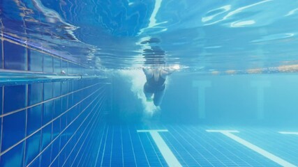 Under water view of professional female swimmer. Woman athlete swimmer training at swimming pool. Underwater view woman dives in pool. Underwater view of girl diving gliding underwater with bubbles