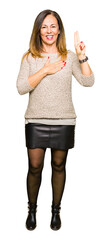 Beautiful middle age woman wearing fashion sweater Swearing with hand on chest and fingers, making...
