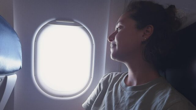Passenger woman is flying in plane. Girl sitting in airplane looking out window going on trip vacation travel. Traveling female inside plane enjoying flight. Traveling girl