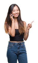 Young asian woman speaking on the phone over isolated background very happy pointing with hand and finger to the side