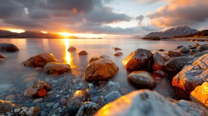 Obraz premium Rocks lie in calm sea water, illuminated by the stunning colors of the sunset. The soft light reflects off the surface of the water, creating a peaceful and picturesque scene.