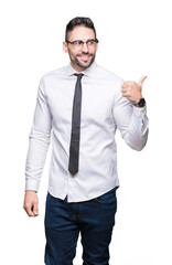 Young handsome business man wearing glasses over isolated background smiling with happy face looking and pointing to the side with thumb up.