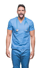 Handsome young doctor surgeon man over isolated background sticking tongue out happy with funny expression. Emotion concept.