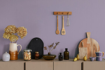 Interior design of kitchen interior with beige shelf, wooden cutboard, glass bottle, vase with flowers, vase with dried flowers, clock and personal accessories. Home decor. Template.
