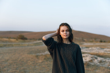 Woman in sweater standing in vast field with hands on head in contemplation