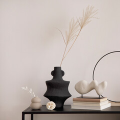 Creative composition of minimalistic interior with black commode vase with dried flowers. White vase with dried flowers and stylish accessories. Beige wall. Home decor. Template.