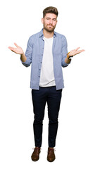 Young handsome blond man wearing casual shirt clueless and confused expression with arms and hands raised. Doubt concept.
