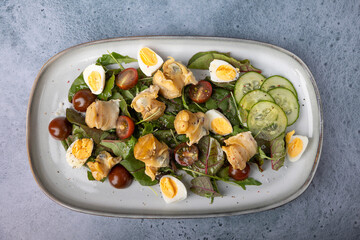 Warm salad with rapan (snails), tomatoes, cucumbers, leafy vegetables, quail eggs and olive oil. Traditional seafood salad. Close-up, selective focus.