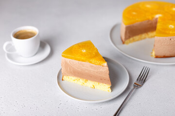 Chocolate-orange mousse cake with biscuit base, jelly and orange circles. Piece of homemade cheesecake and a cup of coffee. Traditional holiday dessert. Selective focus, close-up.
