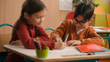 School education studying two funny playing Caucasian little girl daughter child kids children writing in classroom play game drawing fun competition class lesson boy son guy classmates friends write