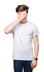 Young handsome man wearing casual white t-shirt over isolated background smiling and laughing with hand on face covering eyes for surprise. Blind concept.