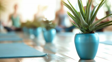 A vibrant blue vase with a green plant placed on a wooden floor surrounded by blurred yoga mats and people in a serene setting.