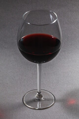 inquadratura verticale, di un calice pieno di vino rosso in primo piano, su sfondo grigio