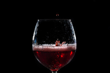goccia che cade all'interno di un calice riempito a metà con del vino rosso su sfondo nero e crea uno schizzo con forme casuali