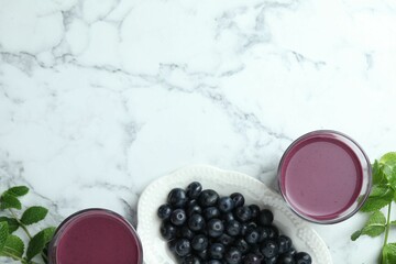 Tasty fresh acai juice in glasses, mint and berries on white marble table, flat lay. Space for text