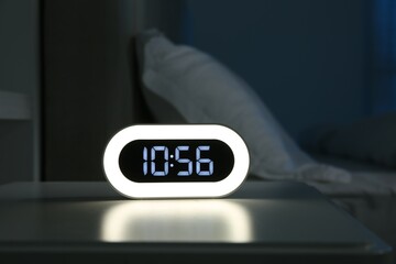 Digital alarm clock on bedside table in bedroom at night
