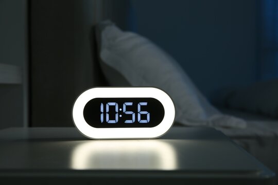 Digital alarm clock on bedside table in bedroom at night