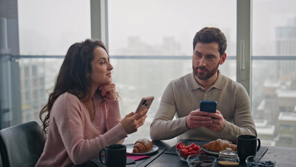 Online pair watching smartphones at kitchen closeup. Couple laughing each other