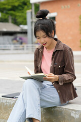 Fototapeta premium A high school student walks outside a school building, looking at her phone. She is smiling and appears engaged with her phone