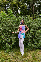 A beautiful young woman in a vibrant dress and sunglasses dances gracefully in a lush green meadow,...